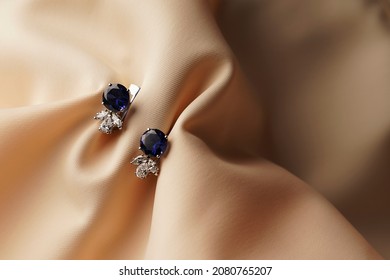 Sapphire Earrings With Diamonds. Pair Of Platinum Earring With Sapphire Gemstone On Beige Satin Background. Luxury Female Jewelry, Close-up