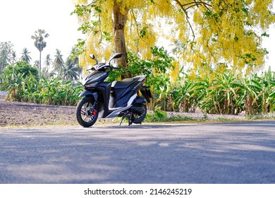 Saraburi, Thailand April 15, 2022 Black Click Motorcycling Motorbike 2021 is on the road and yellow flowers in Thailand.