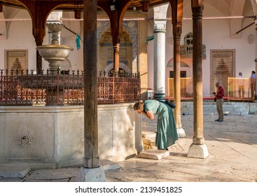 SARAJEVO, BOSNIA AND HERZEGOVINA - July 21, 2021: View from the Gazi Husrev-beg Mosque, a major Islamic building built in the 16th century, showing a woman drinking from the fountain in the courtyard.