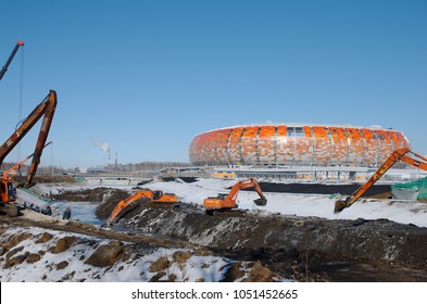 SARANSK, RUSSIA - MARCH 10, 2018: Excavator Cleaning Canal, Mordovia Arena Stadium Visible On The Background.