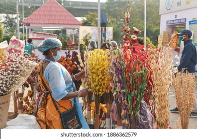 Saras Mela, Kolkata, 12-26-2020: A female artisan (in protective wear due to pandemic) from rural community retail displaying multicolour handmade floral bouquets, made from paper and wooden fibres.