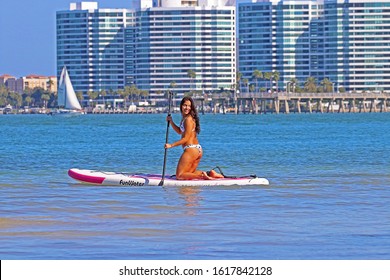 SARASOTA, FLORIDA - JANUARY 13, 2020: A Young Woman Kneeling While Rowing Her FunWater Paddle Board Out Into Sarasota Bay. Stand Up Paddle Boarding Is An Offshoot Of Surfing That Originated In Hawaii.