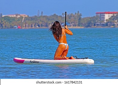 SARASOTA, FLORIDA - JANUARY 13, 2020: A Young Woman Kneeling While Rowing Her FunWater Paddle Board Out Into Sarasota Bay. Stand Up Paddle Boarding Is An Offshoot Of Surfing That Originated In Hawaii.