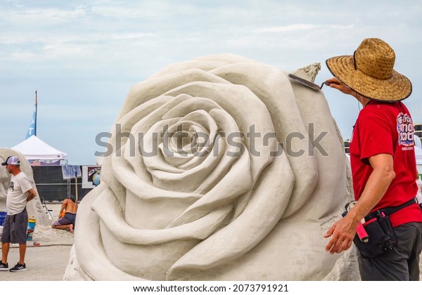 SARASOTA, FLORIDA, USA - NOV. 12, 2021: An artist\
with a trowel smooths part of a floral sculpture in progress Siesta\
Key Crystal Classic, an international sand sculpting festival on\
Siesta Key Beach.