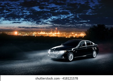 Saratov, Russia - June 12, 2015: Black Car BMW E90 Standing In The Dark Mist Forest With Views Of The City At Night