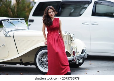 Sarawak, Malaysia – March 31 2013: The Photo Showing Portrait Of A Young Beautiful Asian Woman Or Girl In Red Evening Dress Leaning Against The Retro Car At Carpark.                              