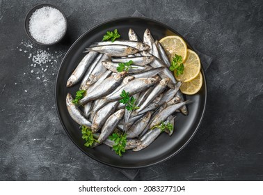 Sardines with lemon, salt and parsley close-up on a dark background. Sea fish. Top view.