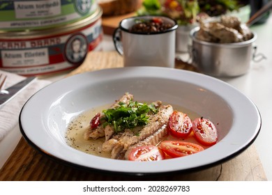 Sardines In Olive Oil, Tomatoes, Herbs In An Enameled Dish On Wood. Sardine Cans, Mug And Salad In The Background