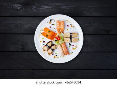 Sashimi Set On A White Round Plate, Decorated With Small Flowers, Japanese Food, Top View. Black Wooden Background