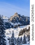 Sassongher mountain rises above a snow covered valley in the Dolomites, Italy. Small wooden cabins are scattered across the hills, creating a peaceful alpine winter scene (Vertical photo)