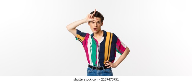 Sassy And Arrogant Guy Showing Loser Sign On Forehead, Mocking Someone, Standing Over White Background