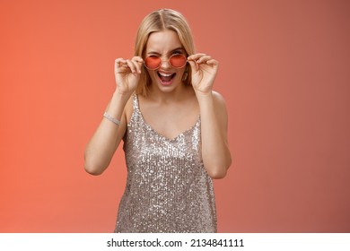 Sassy carefree daring young blond girl winking cheeky smiling assertive making first move approach handsome man nightclub asking dance standing red background touching sunglasses wear dress