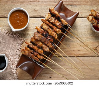 Satay ayam or sate ayam is Indonesian food and cuisine of seasoned, skewered and grilled chicken with palm stick served with peanut, soy and chili sauce.Serving on wooden table and brown food burner
