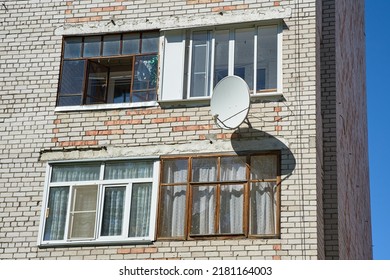A satellite dish is hanging on the wall of a brick house