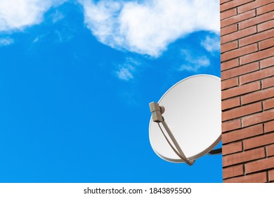 Satellite dish on brick wall against blue sky