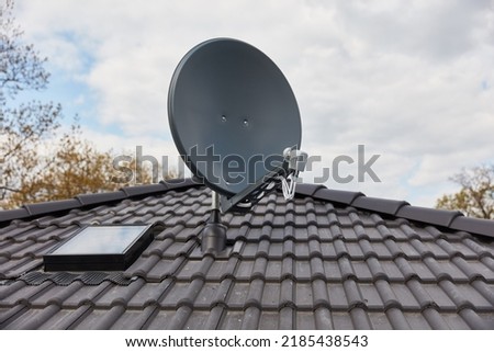 Satellite dish on the roof of the house next to the skylight for maintenance and care of the satellite system