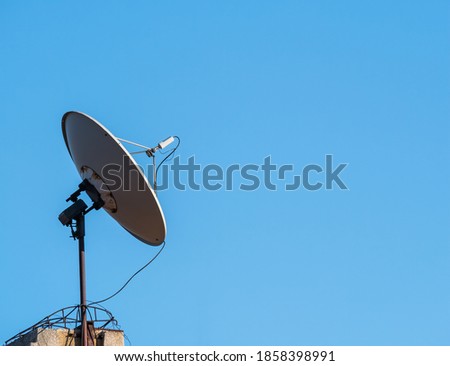 Satellite dish or parabolic antenna on the roof of a building against blue sky.