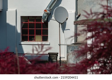 Satellite dish in the yard of a workshop and ventilation pipe through the mesh window - blurry reddish foreground