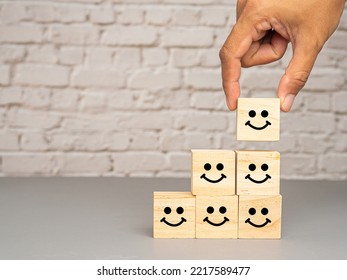 Satisfaction concept. Side view of wooden cubes with stacked smile icons over a table with white brick wall background. Happy mood icons. Feedback emotion scale