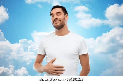 Satisfaction, Healthy Eating And People Concept - Happy Full Man Touching His Tummy Over Blue Sky And Clouds Background