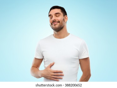 Satisfaction, Healthy Eating And People Concept - Happy Full Man Touching His Tummy Over Blue Background