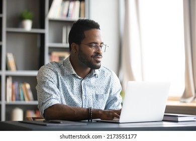 Satisfied African American man wearing glasses looking at computer screen, reading good news in email, chatting in social network with friends, freelancer blogger working on online project - Shutterstock ID 2173551177