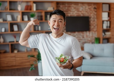 Satisfied asian mature man in sportswear holding bowl with fresh salad and showing biceps, resting and eating after domestic workout. Diet, motivation and weight loss - Powered by Shutterstock