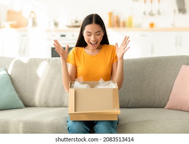 Satisfied asian woman opening cardboard box, excited over great delivery service, receiving online shop order, sitting on sofa at home, free space. Young lady unpacking parcel at living room - Powered by Shutterstock