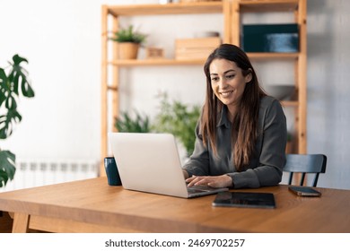 Satisfied beautiful millennial woman typing on laptop computer while sitting at table in home office. - Powered by Shutterstock