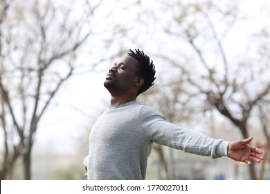 Satisfied black man breathing fresh air with eyes closed standing in the park outdoors 