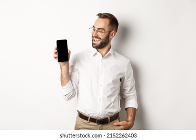 Satisfied Business Man Showing And Looking At Mobile Screen, Introduce Application Or Website Promo, Standing Over White Background