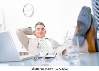 Satisfied Businessman Sitting By Desk At Office, Feet On Table, Smiling, Looking At Camera.