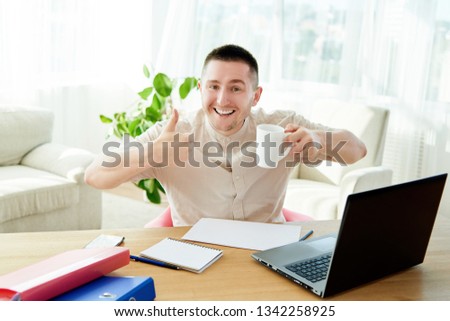 Satisfied businessman with work done in office with cup of coffee. Happy young man working on laptop while sitting at workingplace