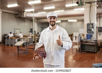 A satisfied butcher holds a peace of fresh meat and approves of quality while standing in the meat factory and smiling at the camera. - Powered by Shutterstock