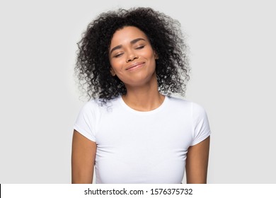 Satisfied Calm African American Woman Enjoying Fresh Air, Good Smell, Dreaming About Future With Closed Eyes, Smiling Pleased Peaceful Young Female With Curly Hair Isolated On Studio Background