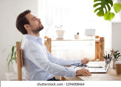 Satisfied calm businessman taking break to relax finished work sitting at desk enjoying stress free job breathing fresh air, happy executive manager resting at workplace dreaming in quiet office