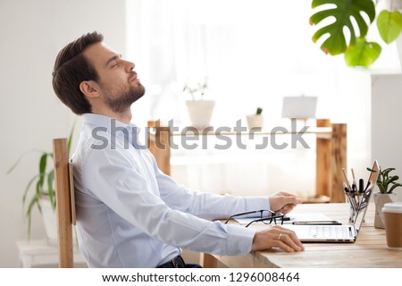 Satisfied calm businessman taking break to relax finished work sitting at desk enjoying stress free job breathing fresh air, happy executive manager resting at workplace dreaming in quiet office