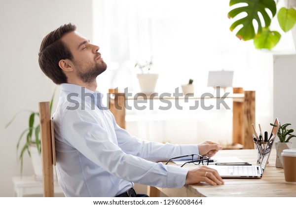 Satisfied calm businessman taking break to relax\
finished work sitting at desk enjoying stress free job breathing\
fresh air, happy executive manager resting at workplace dreaming in\
quiet office