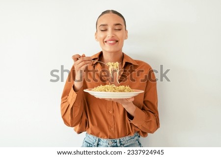 Satisfied caucasian lady enjoying tasty Italian spaghetti with closed eyes, standing on white studio background wall. Italian cuisine concept. Pasta lover