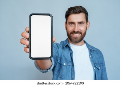 Satisfied confident smiling caucasian man showing mobile phone blank white screen mockup to camera standing isolated on blue studio copy space. Closeup smartphone in male hand. Advertisement concept - Shutterstock ID 2064922190