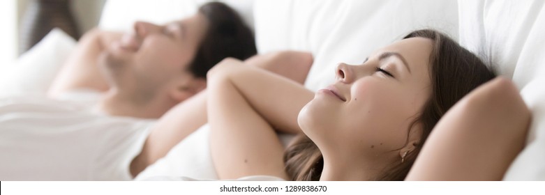 Satisfied couple sleeping lying in bed, close up focus on wife closed eyes putting hands behind head feels good after healthy rest or sex with husband horizontal photo banner for website header design