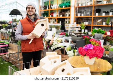 a satisfied customer in a garden and garden supply store holds a birdhouse in his hands