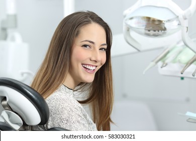 Satisfied dentist patient showing her perfect smile after treatment in a clinic box with medical equipment in the background - Powered by Shutterstock