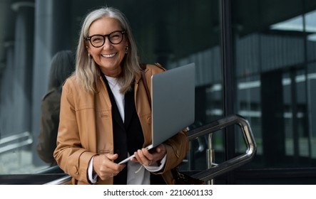 satisfied elderly businesswoman with a wide smile and a laptop in her hands against the backdrop of the office center