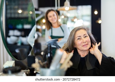 Satisfied elderly female client sitting in hairdressing chair after haircut from professional stylist. - Powered by Shutterstock