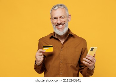 Satisfied elderly gray-haired man 40s years old wears brown shirt using mobile cell phone hold credit bank card doing online shopping order delivery isolated on plain yellow background studio portrait - Powered by Shutterstock