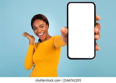 Satisfied excited pretty young african american female in yellow t-shirt show smartphone with blank screen, isolated on blue background. Blogger recommendation, great offer, huge sale and website - Powered by Shutterstock