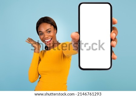 Satisfied excited pretty young african american female in yellow t-shirt show smartphone with blank screen, isolated on blue background. Blogger recommendation, great offer, huge sale and website