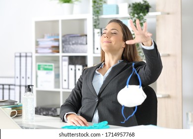 Satisfied executive woman breathing fresh air throwing protective mask on a desk at the office