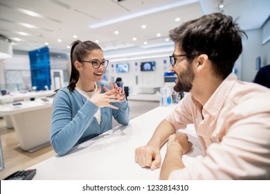 Satisfied Female Customer On The Cashier Talking To Man That Working At Tech Store.